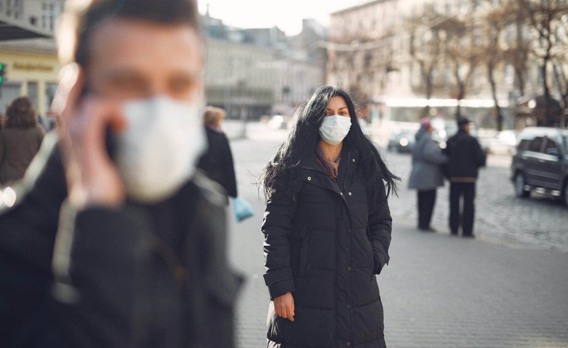 woman in a black coat and face mask standing on street