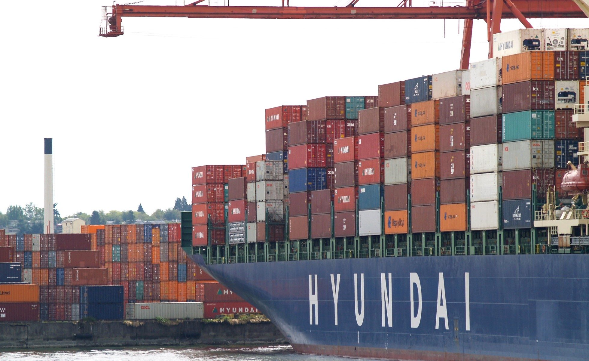 Shipping containers stacked near a port. Blue Hyundai tanker is in the foreview.