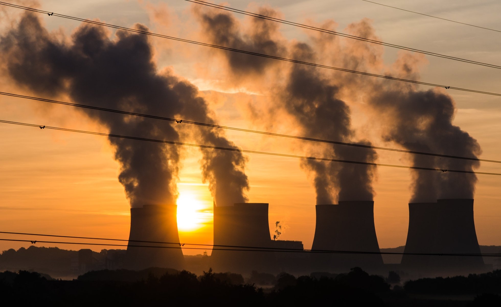 four smoke stacks up against a a sunset with powerlines in the foreview